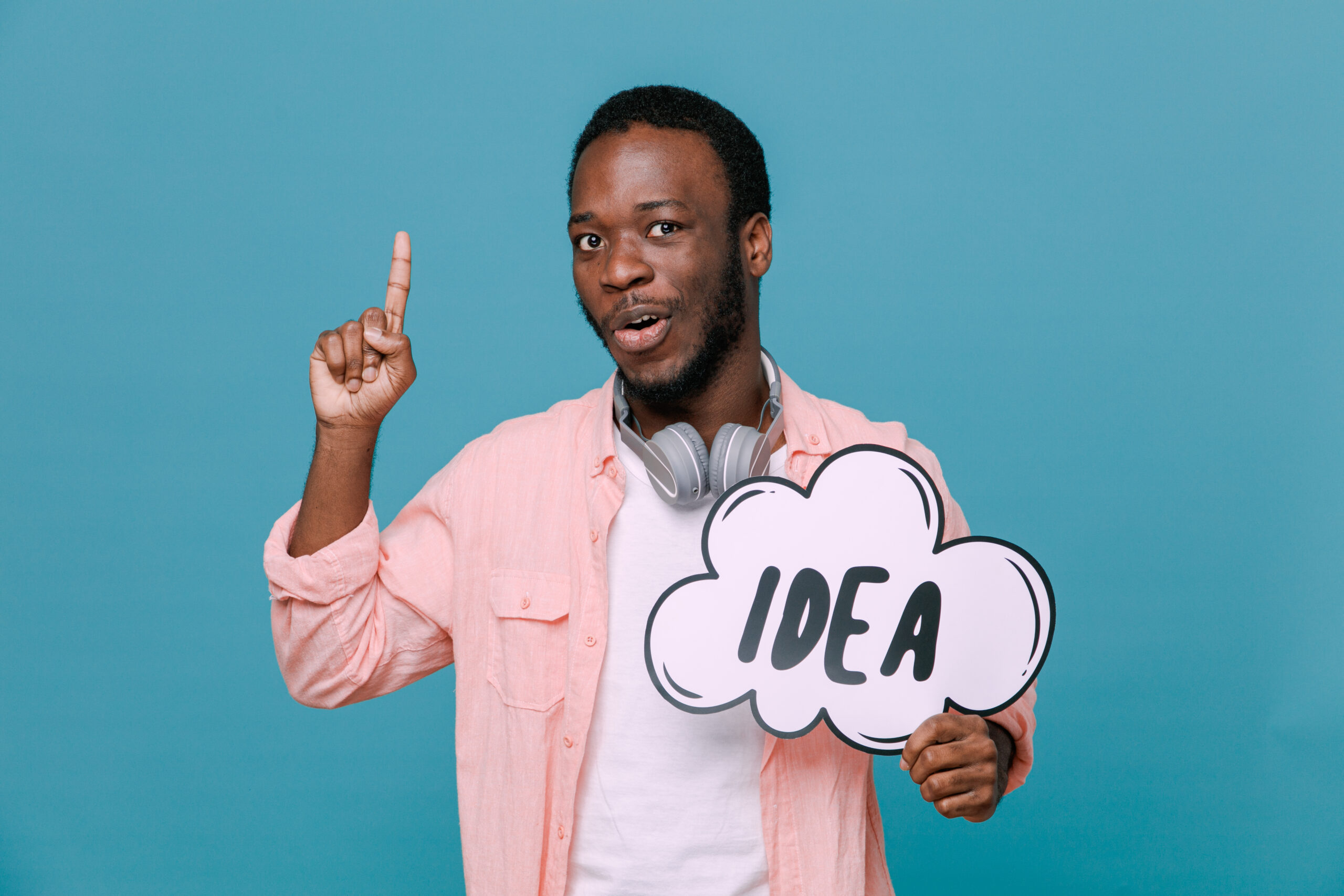 Home impressed points at up holding idea bubble young africanamerican guy wearing headphones on neck isolated on blue background